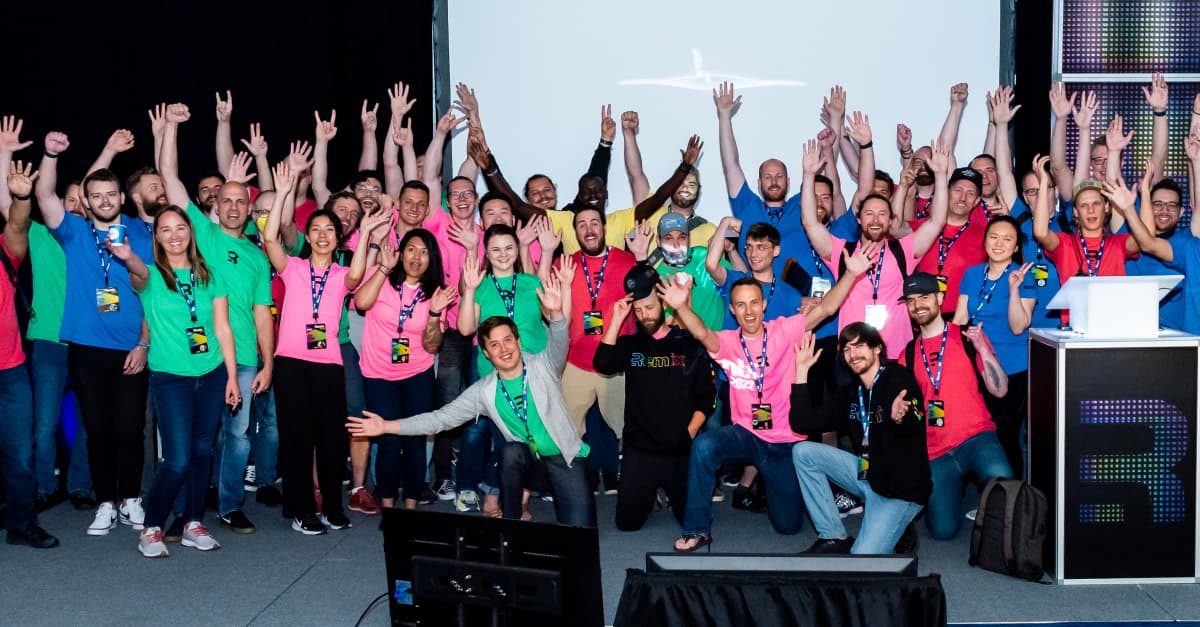Dozens of Remix Conf attendees in colorful remix shirts with their hands up in the air